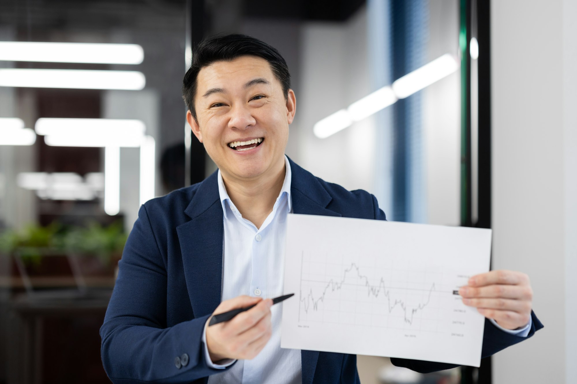 Cheerful taiwan investor showing sheet of paper with growing statistics and pointing with pen to